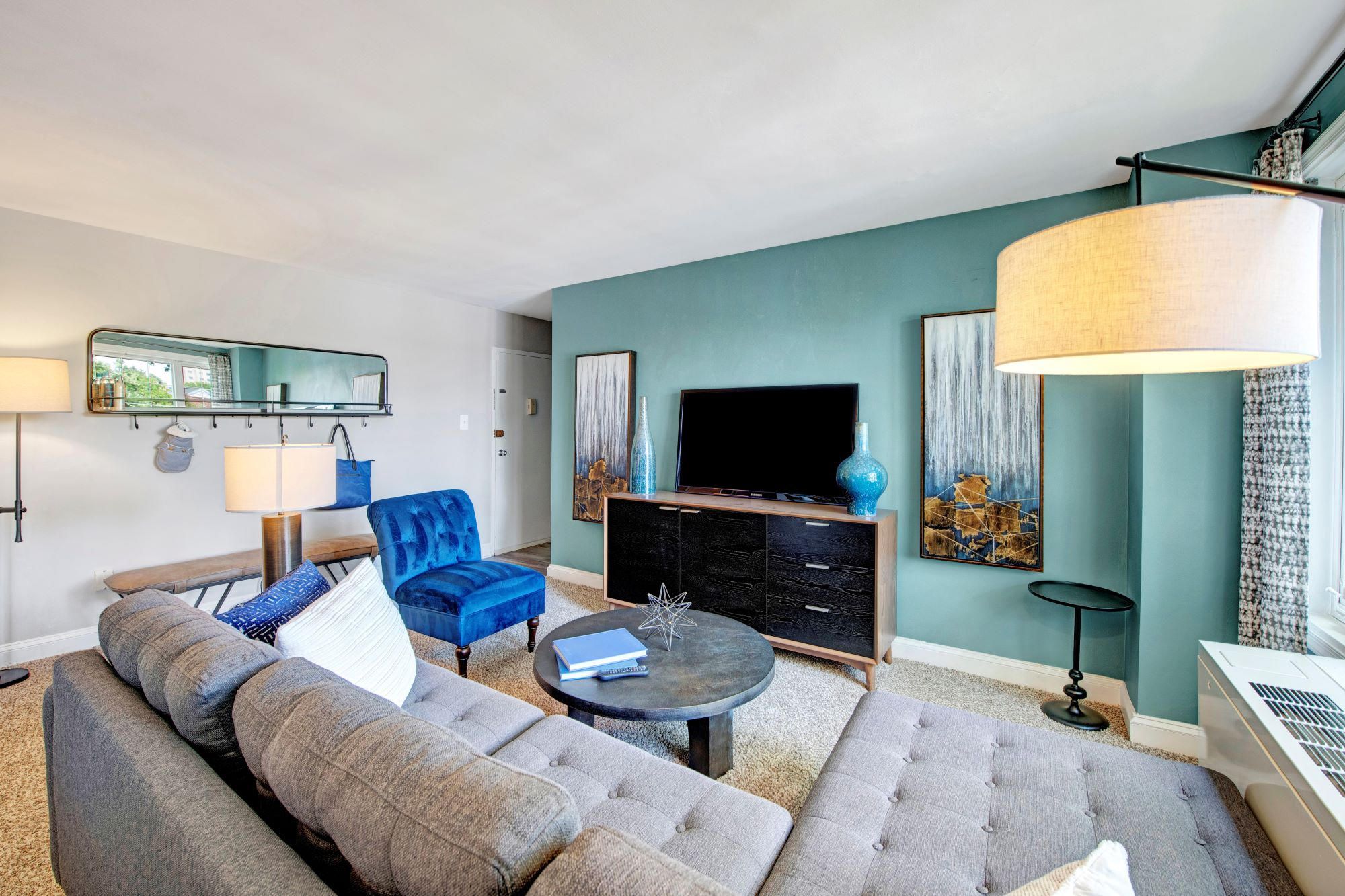 Modern living room with blue accent wall, gray sofa, blue chair, TV, and large floor lamp.