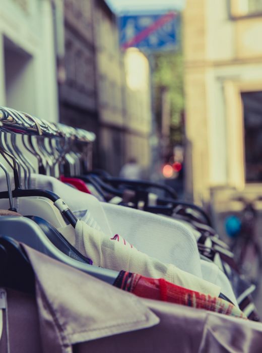 Clothes hanging on a rack outdoors along a city street, with buildings in the background.