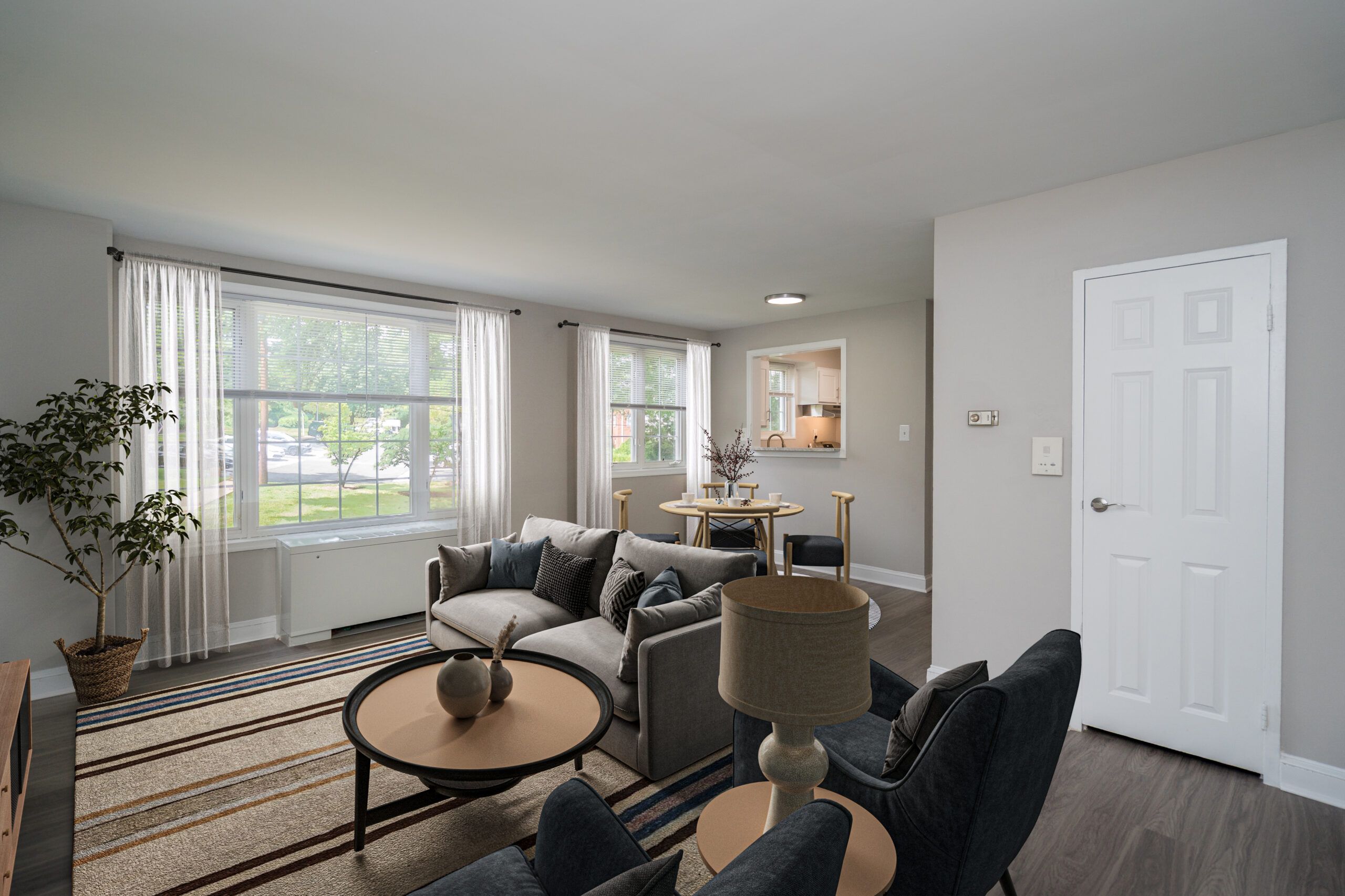 A staged living room with a sofa, coffee table, armchair, dining set, and a view through the window.