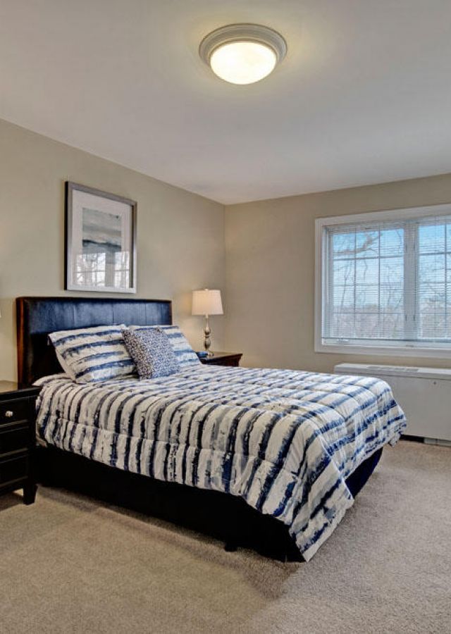 Bedroom with a double bed, striped bedding, two nightstands, lamps, and a window letting in natural light.