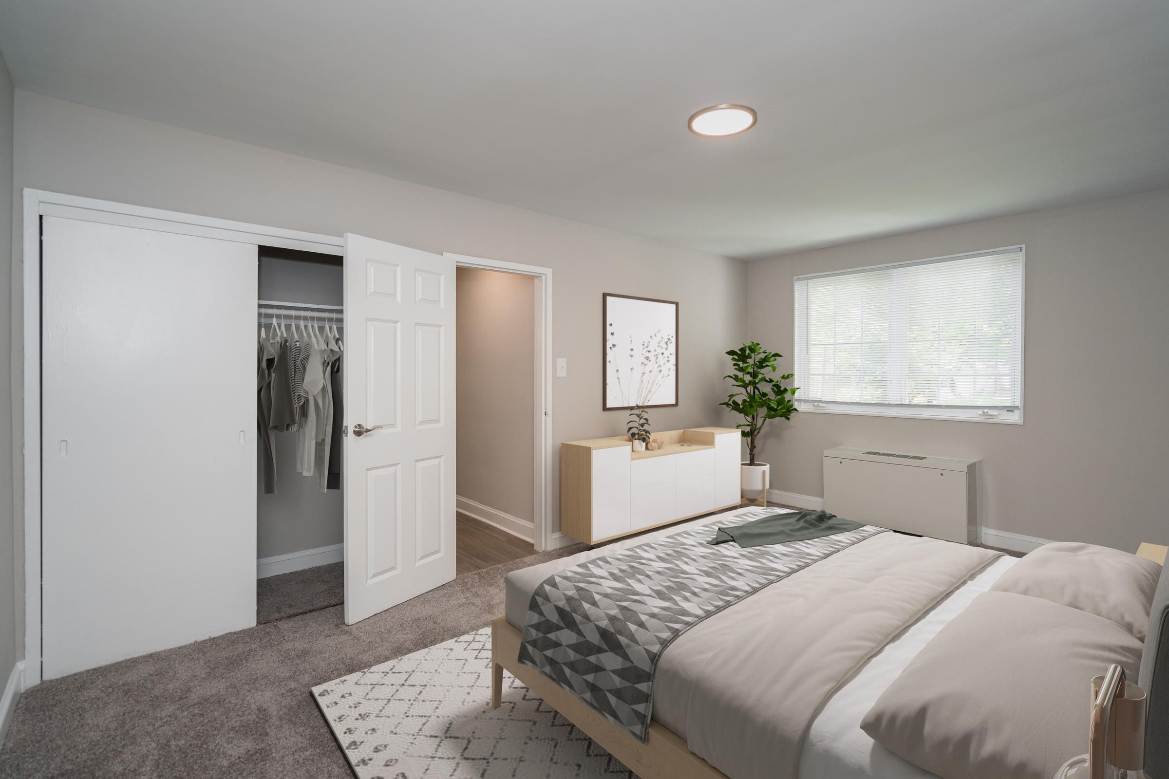 Modern bedroom with open closet, bed, dresser, plant, and large window letting in natural light.